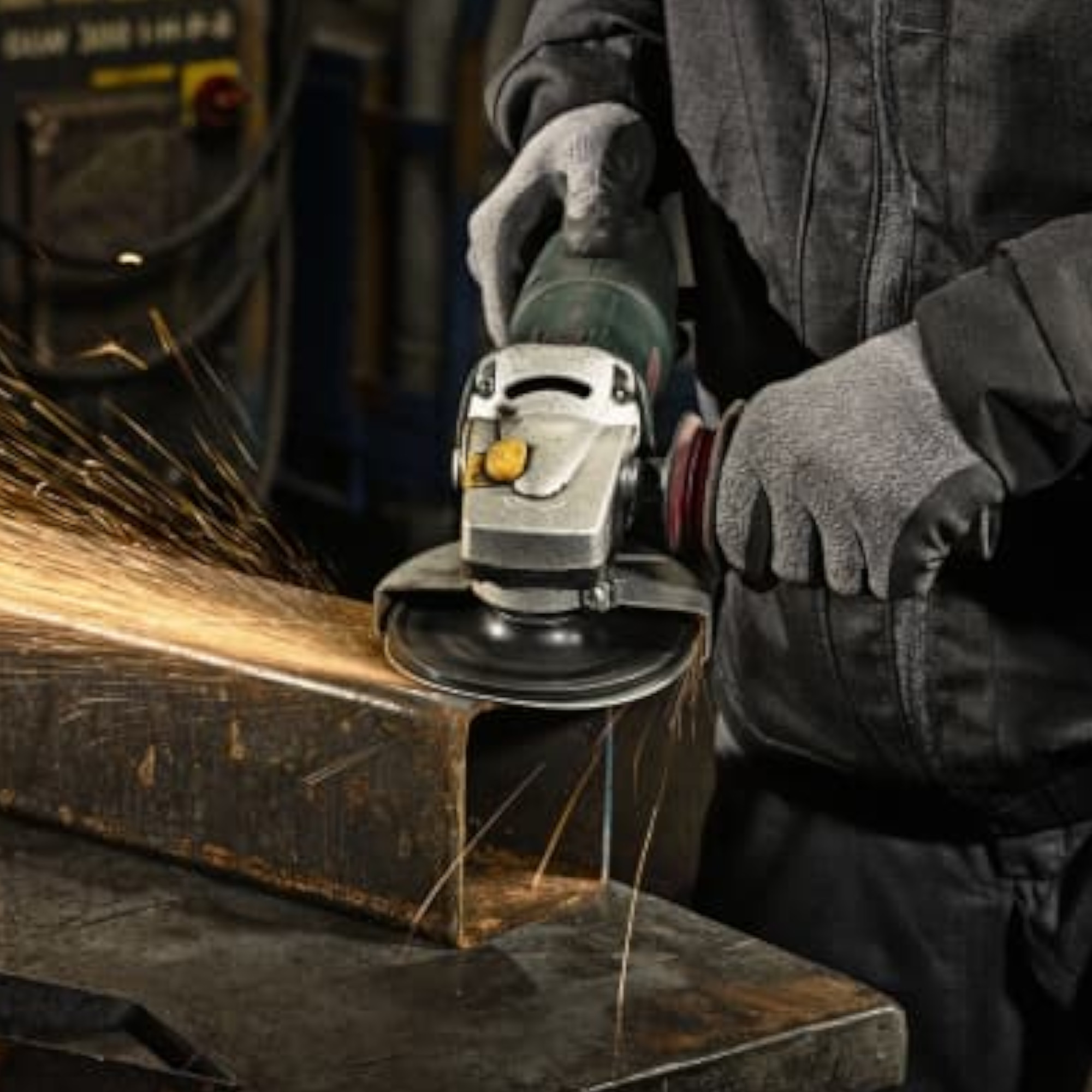Ein Handwerker trägt Handschuhe und benutzt eine Winkelschleifmaschine, um ein Metallstück zu bearbeiten. Funken fliegen von der Schnittstelle, während die Maschine in Betrieb ist. Der Hintergrund zeigt eine Werkstattumgebung.